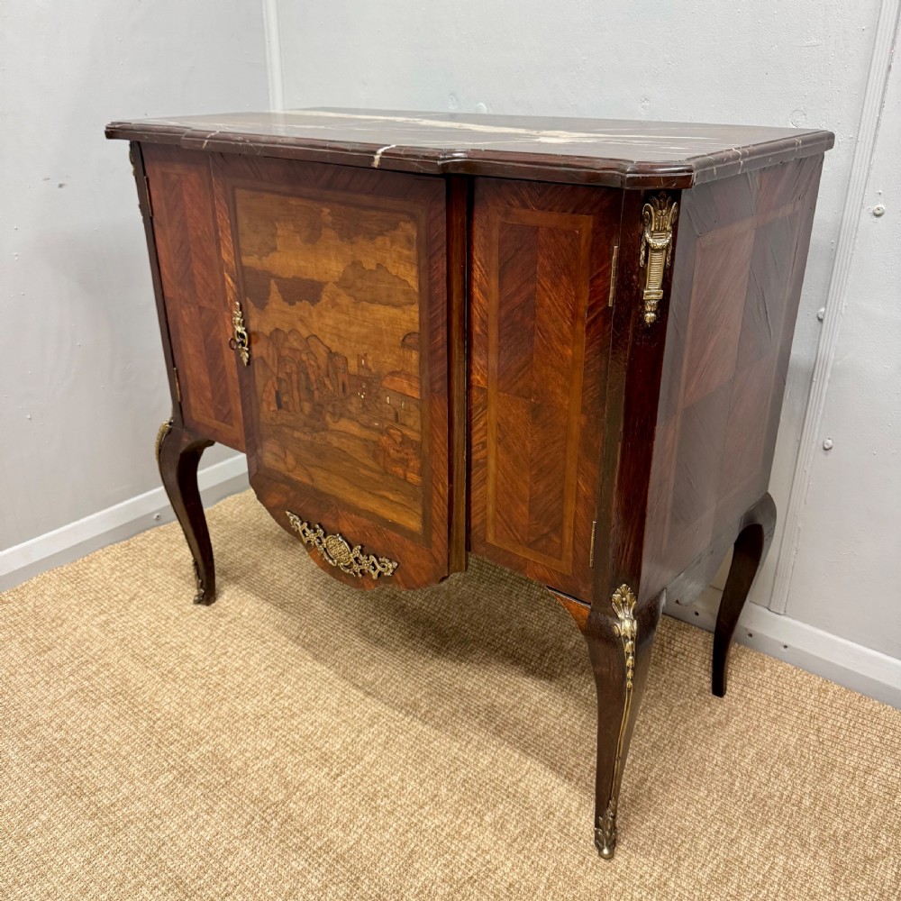An early nineteenth-century French style marquetry commode cabinet with a marble top, cabriole legs, central inlaid architectural landscape scene, and decorative brass mounts. View III
