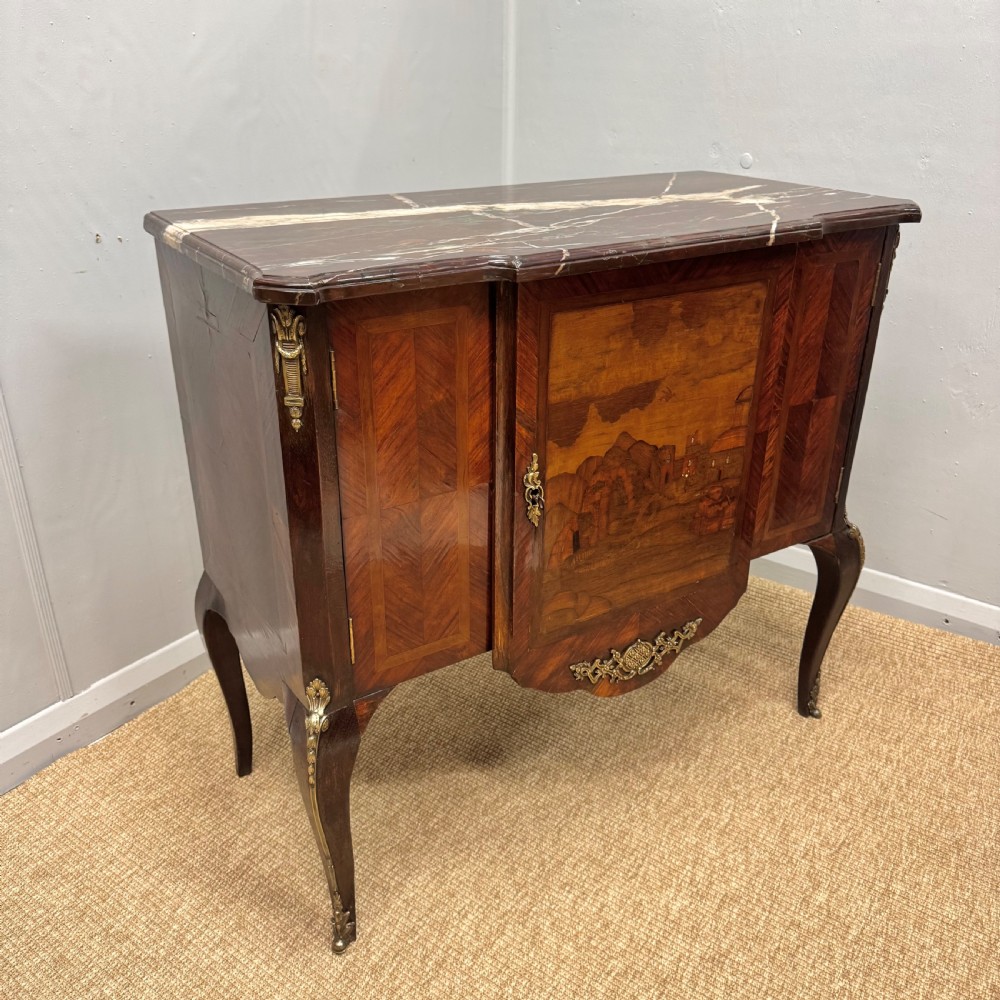 An early nineteenth-century French style marquetry commode cabinet with a marble top, cabriole legs, central inlaid architectural landscape scene, and decorative brass mounts. View IV