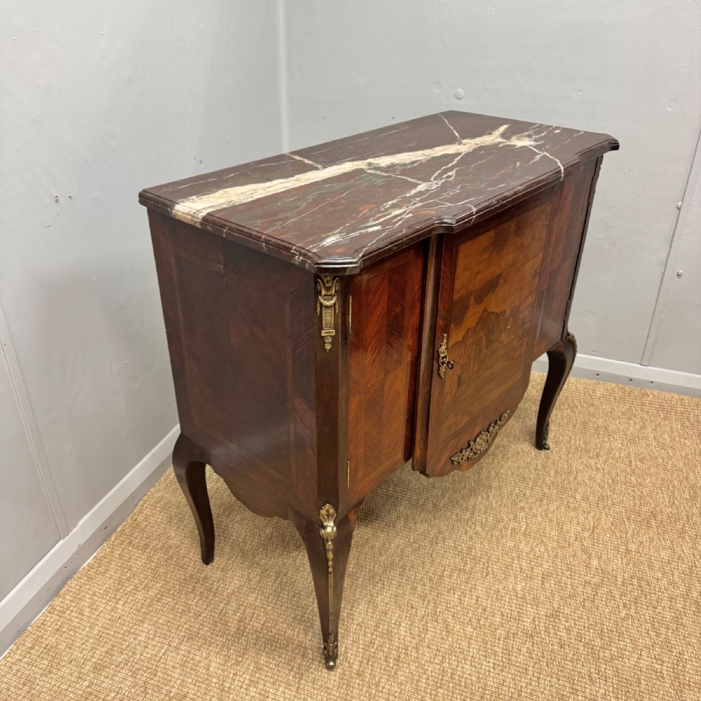 An early nineteenth-century French style marquetry commode cabinet with a marble top, cabriole legs, central inlaid architectural landscape scene, and decorative brass mounts. View V