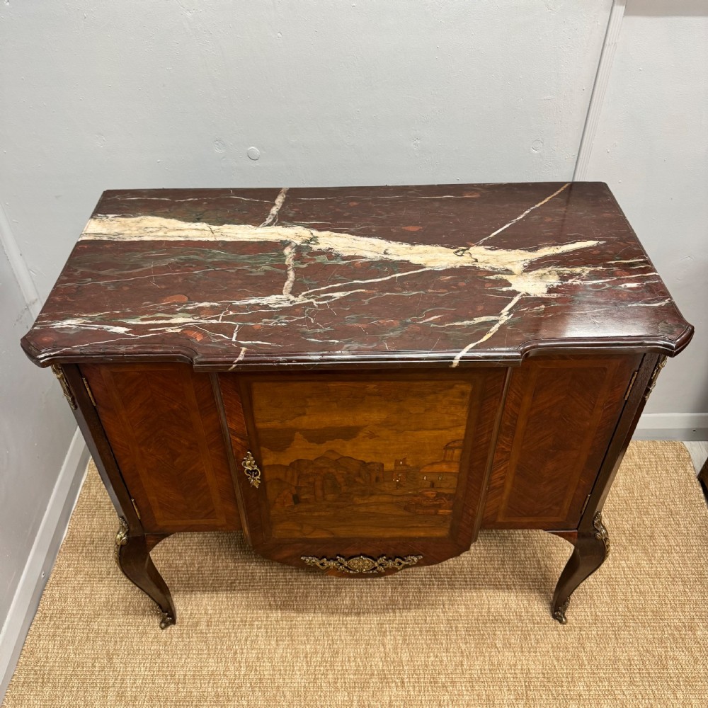 An early nineteenth-century French style marquetry commode cabinet with a marble top, cabriole legs, central inlaid architectural landscape scene, and decorative brass mounts. View VIII