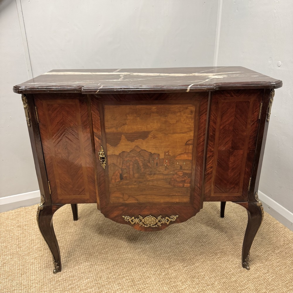 An early nineteenth-century French style marquetry commode cabinet with a marble top, cabriole legs, central inlaid architectural landscape scene, and decorative brass mounts.