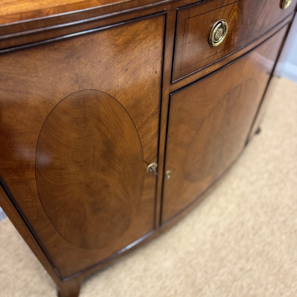 A mahogany bow front glazed bookcase cabinet featuring geometric astragal glazing bars above a cupboard base with flame veneer panels. View IV