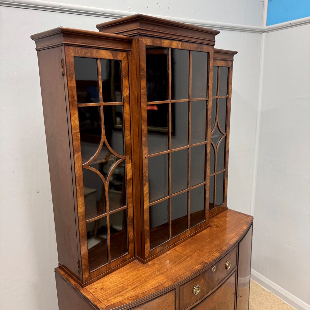 A mahogany bow front glazed bookcase cabinet featuring geometric astragal glazing bars above a cupboard base with flame veneer panels. View V