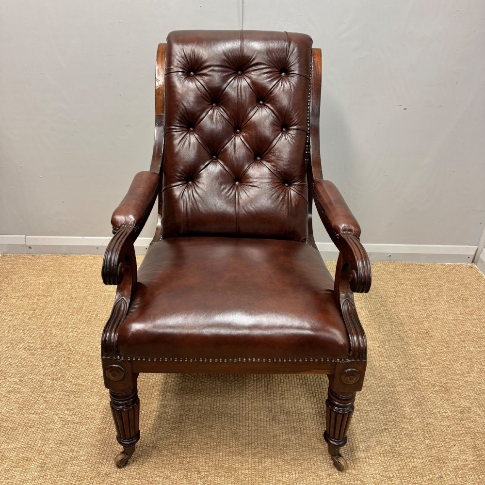 A Georgian mahogany armchair upholstered in deep brown buttoned leather with padded scroll arms, brass studded trim, and fluted front legs on castors. View III