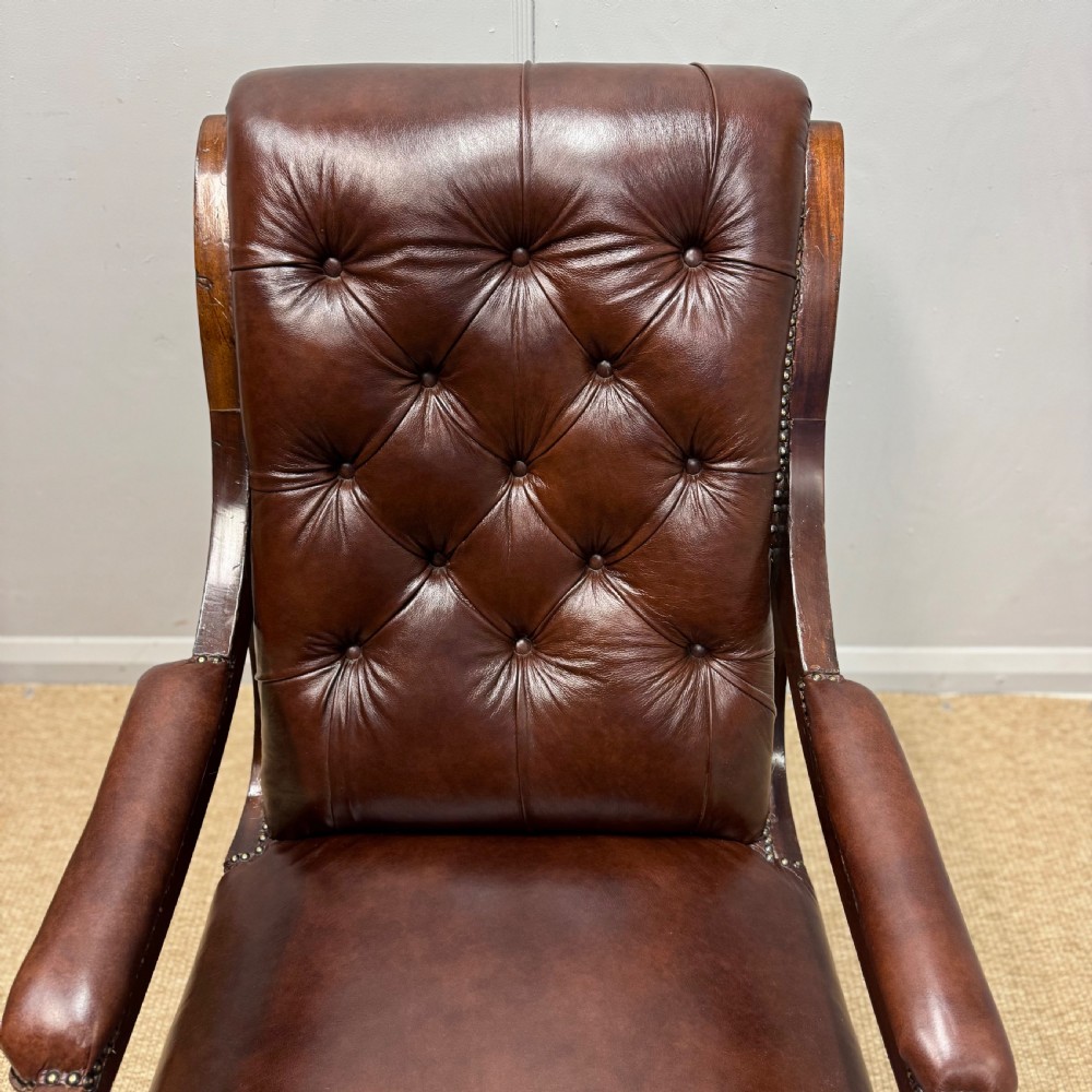 A Georgian mahogany armchair upholstered in deep brown buttoned leather with padded scroll arms, brass studded trim, and fluted front legs on castors. View IV