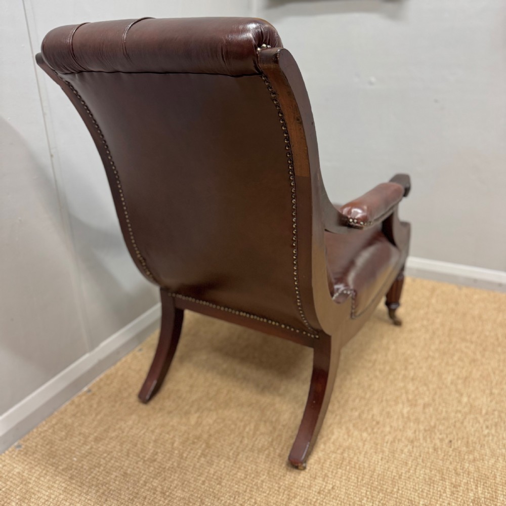 A Georgian mahogany armchair upholstered in deep brown buttoned leather with padded scroll arms, brass studded trim, and fluted front legs on castors. View VI