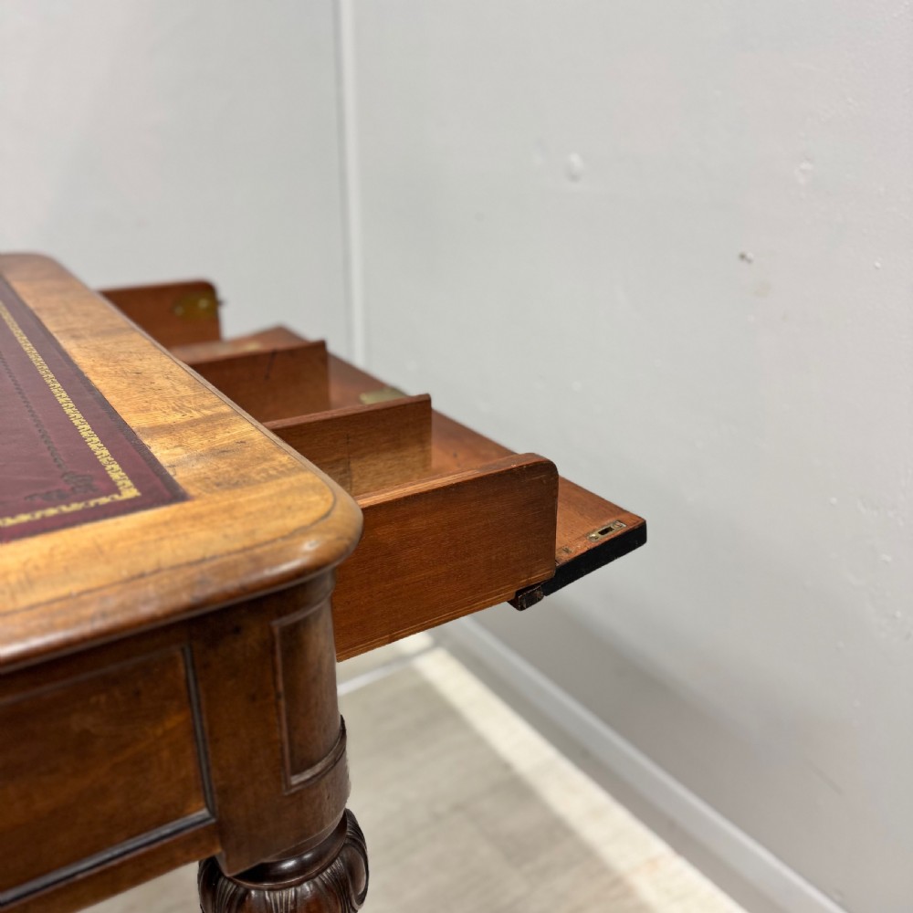 A Regency mahogany library table featuring an inset burgundy leather writing surface, turned fluted legs on brass castors, and a side drawer with brass knobs. View II