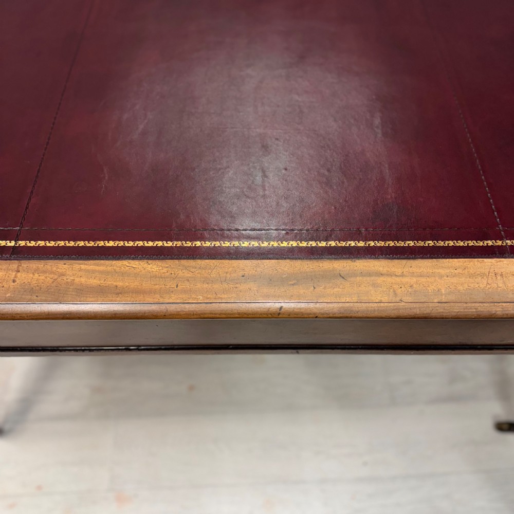 A Regency mahogany library table featuring an inset burgundy leather writing surface, turned fluted legs on brass castors, and a side drawer with brass knobs. View III