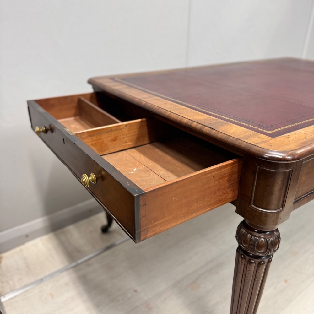 A Regency mahogany library table featuring an inset burgundy leather writing surface, turned fluted legs on brass castors, and a side drawer with brass knobs. View V