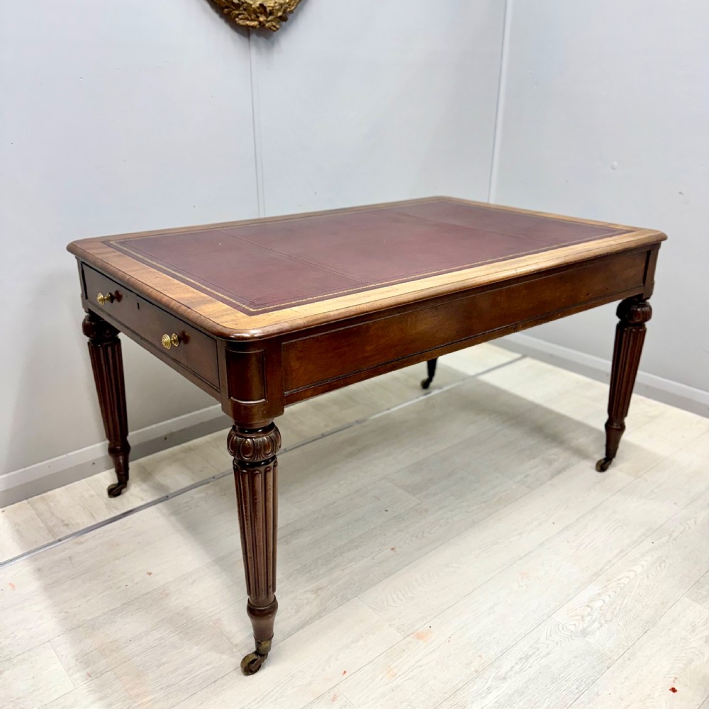 A Regency mahogany library table featuring an inset burgundy leather writing surface, turned fluted legs on brass castors, and a side drawer with brass knobs.