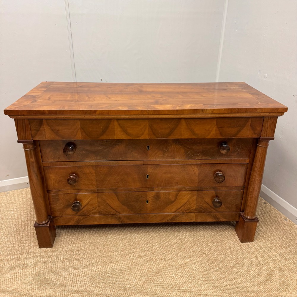 A 19th-century French cherry wood commode featuring three lower drawers with turned knobs, a top frieze drawer, and side columns on block feet.