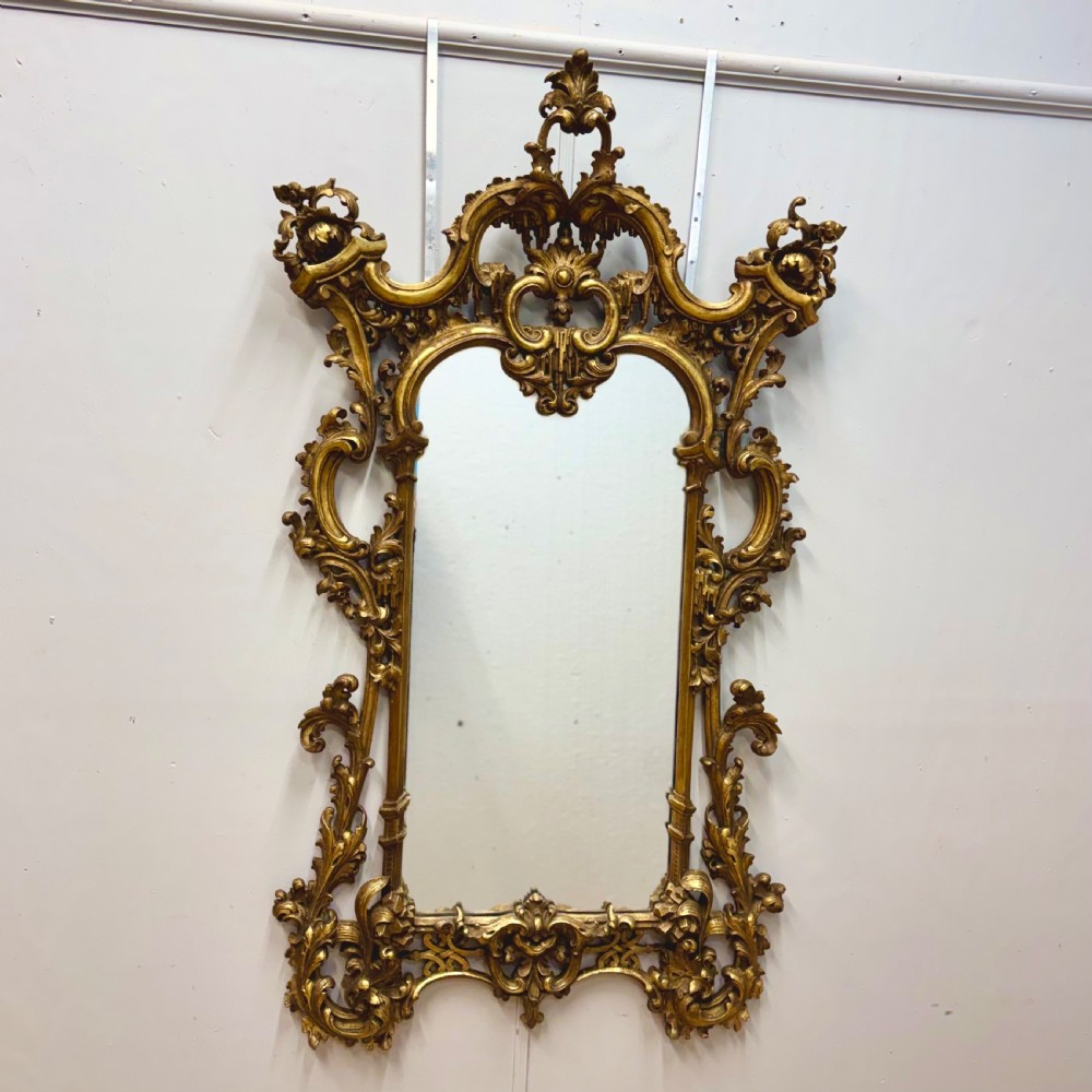 An ornate 18th-century carved giltwood wall mirror featuring elaborate rococo scrolling acanthus leaves and a central arched frame.