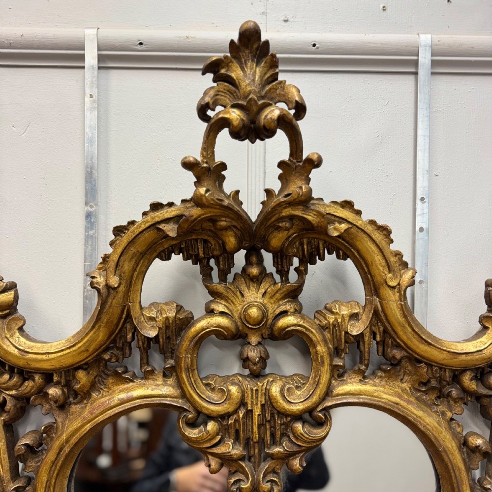 An ornate 18th-century carved giltwood wall mirror featuring elaborate rococo scrolling acanthus leaves and a central arched frame. View II