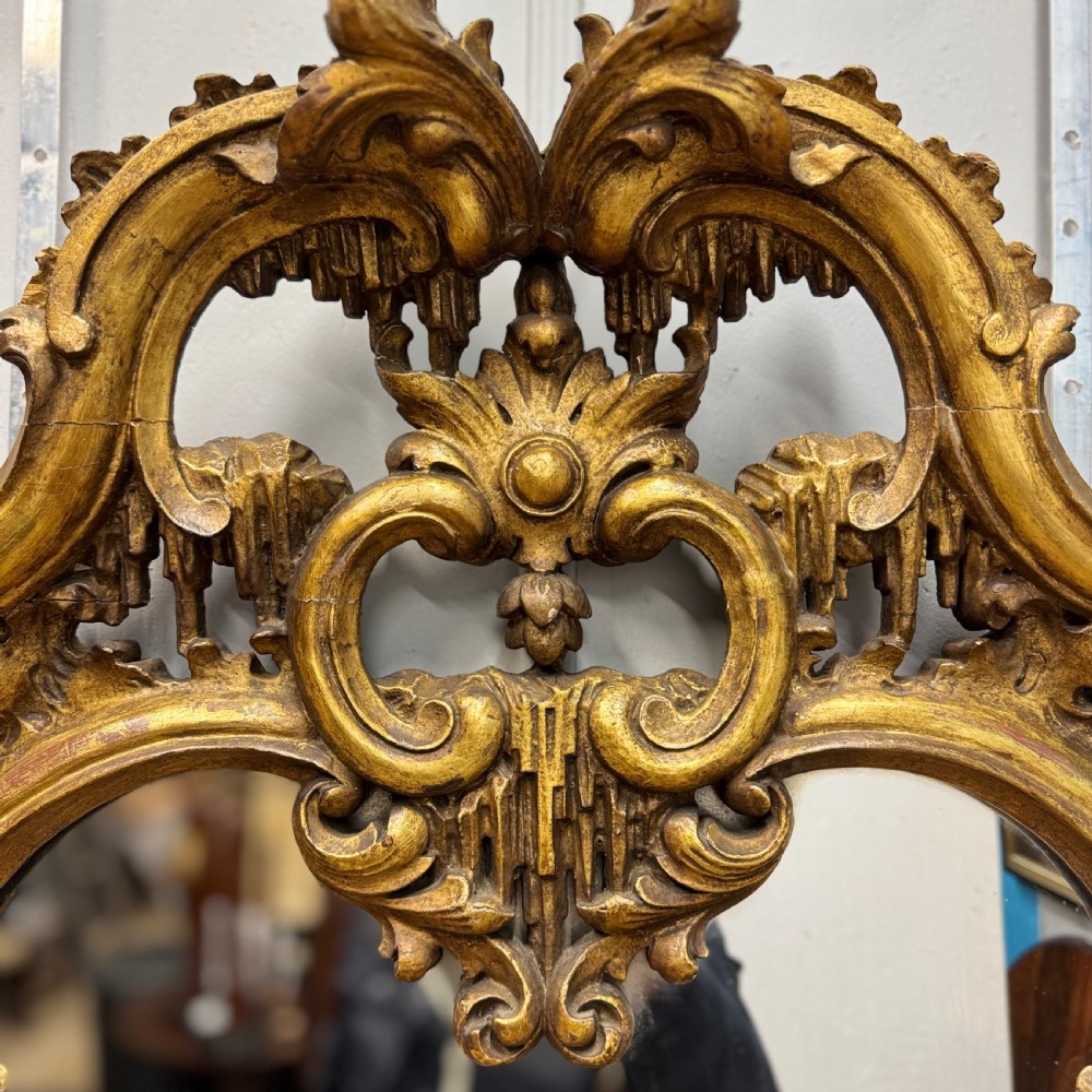 An ornate 18th-century carved giltwood wall mirror featuring elaborate rococo scrolling acanthus leaves and a central arched frame. View III