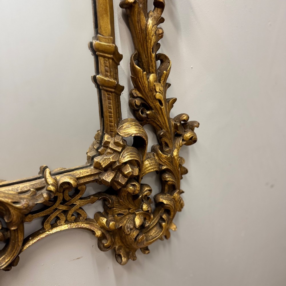 An ornate 18th-century carved giltwood wall mirror featuring elaborate rococo scrolling acanthus leaves and a central arched frame. View V