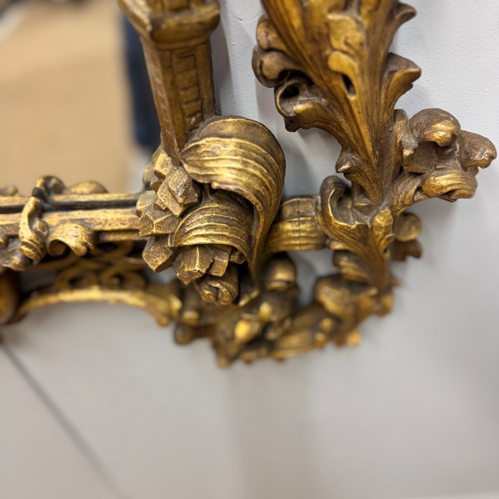 An ornate 18th-century carved giltwood wall mirror featuring elaborate rococo scrolling acanthus leaves and a central arched frame. View VI