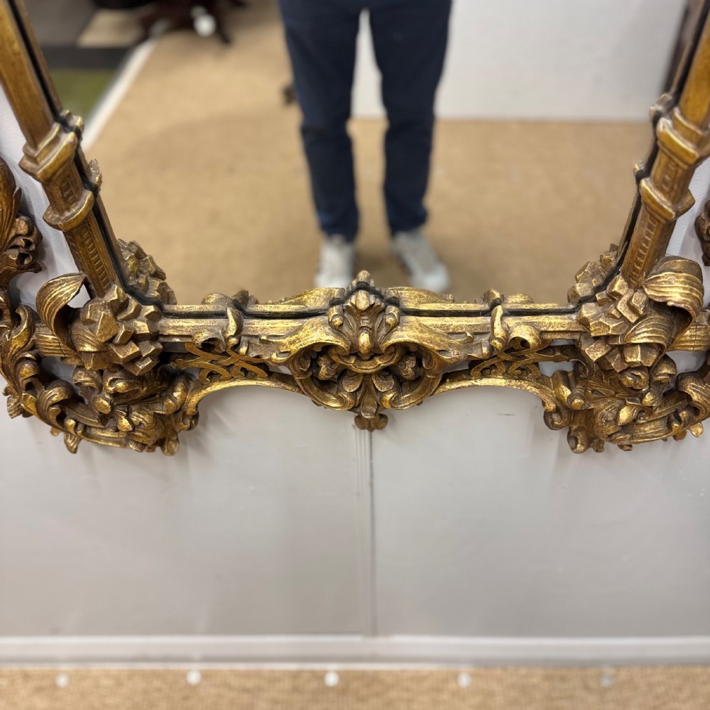An ornate 18th-century carved giltwood wall mirror featuring elaborate rococo scrolling acanthus leaves and a central arched frame. View VII