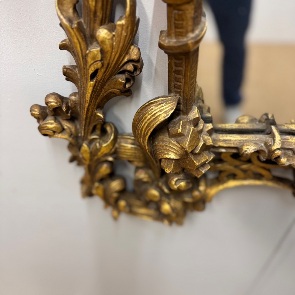 An ornate 18th-century carved giltwood wall mirror featuring elaborate rococo scrolling acanthus leaves and a central arched frame. View VIII