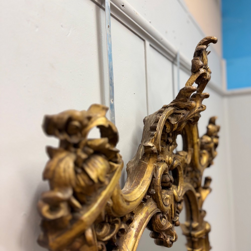An ornate 18th-century carved giltwood wall mirror featuring elaborate rococo scrolling acanthus leaves and a central arched frame. View IX