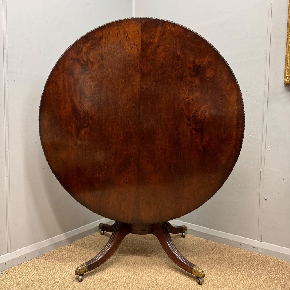 A circular Georgian plum pudding mahogany centre table shown in a tilted position on a reeded pedestal with four splayed legs and brass castors.