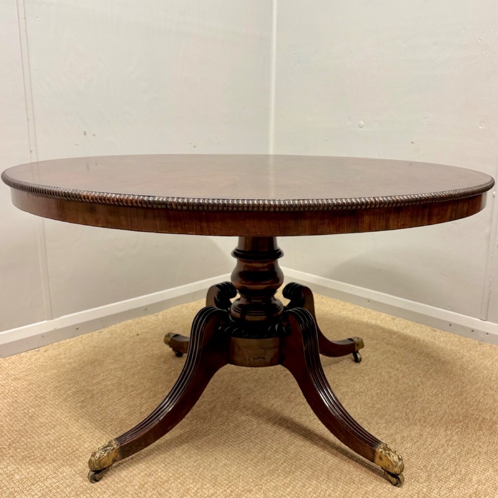 A circular Georgian plum pudding mahogany centre table shown in a tilted position on a reeded pedestal with four splayed legs and brass castors. View III