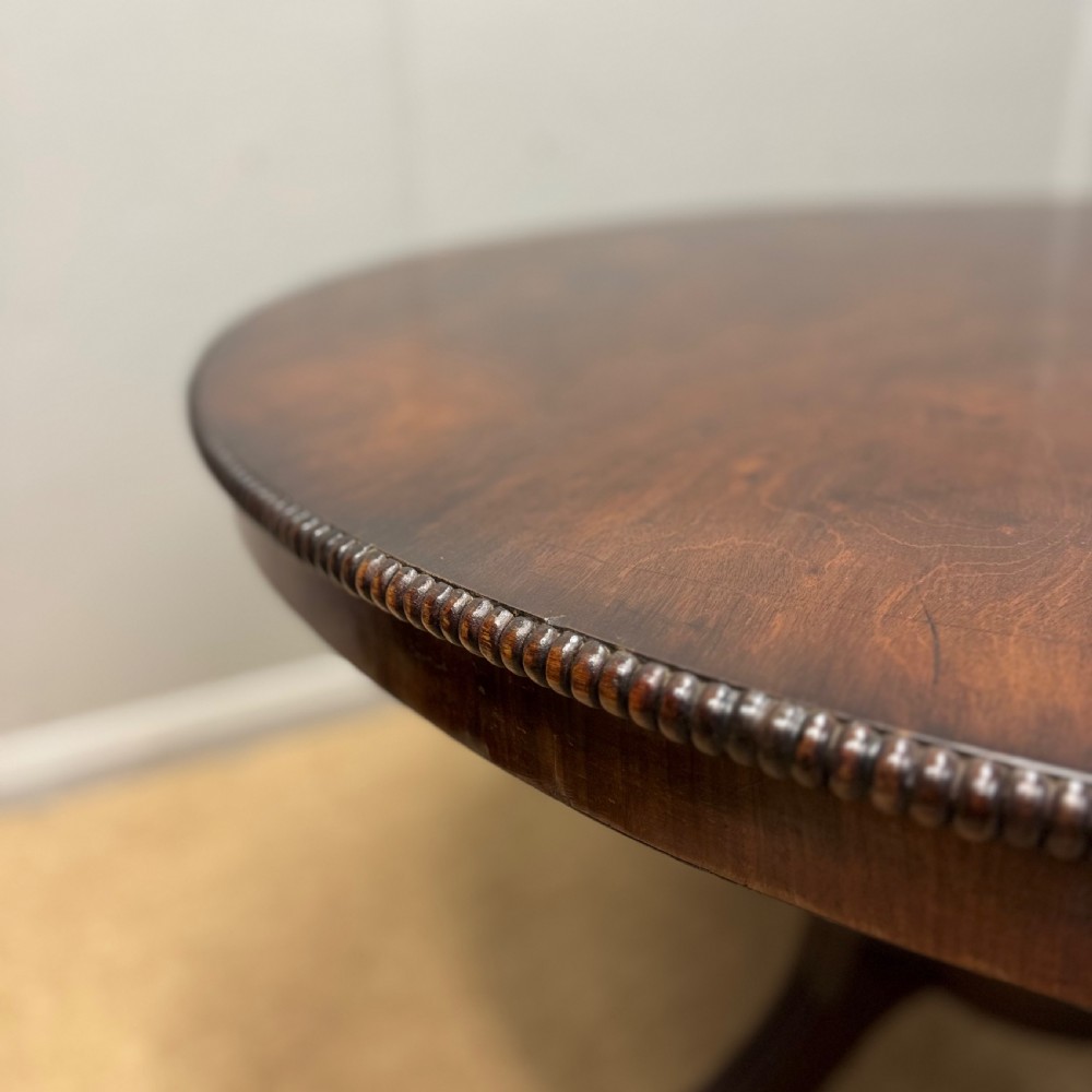 A circular Georgian plum pudding mahogany centre table shown in a tilted position on a reeded pedestal with four splayed legs and brass castors. View IV