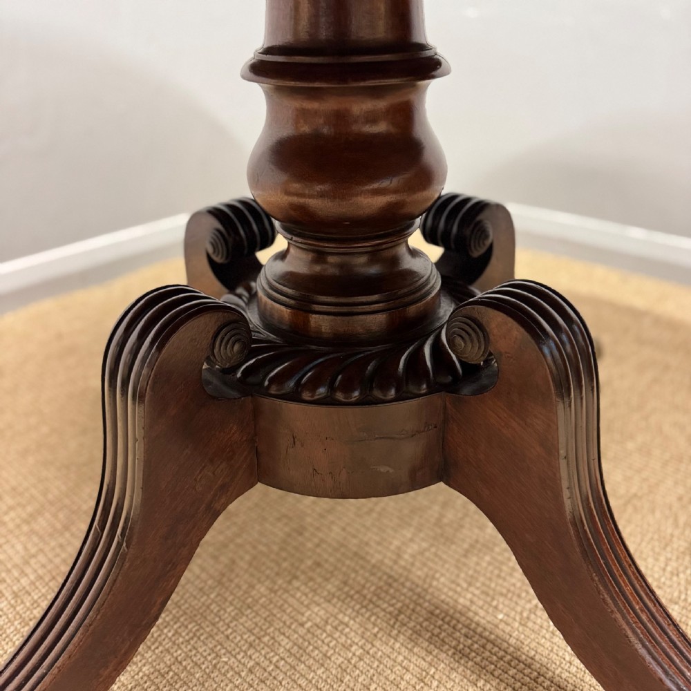 A circular Georgian plum pudding mahogany centre table shown in a tilted position on a reeded pedestal with four splayed legs and brass castors. View V