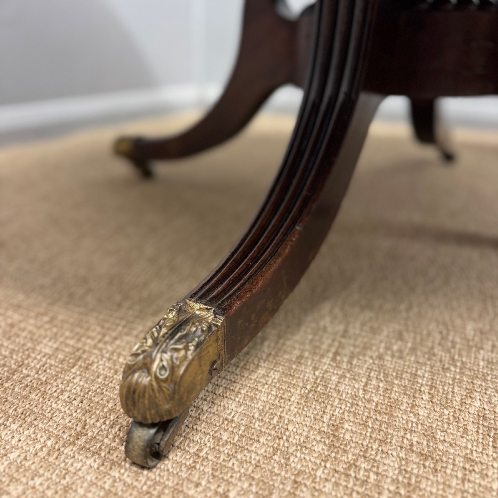 A circular Georgian plum pudding mahogany centre table shown in a tilted position on a reeded pedestal with four splayed legs and brass castors. View VI