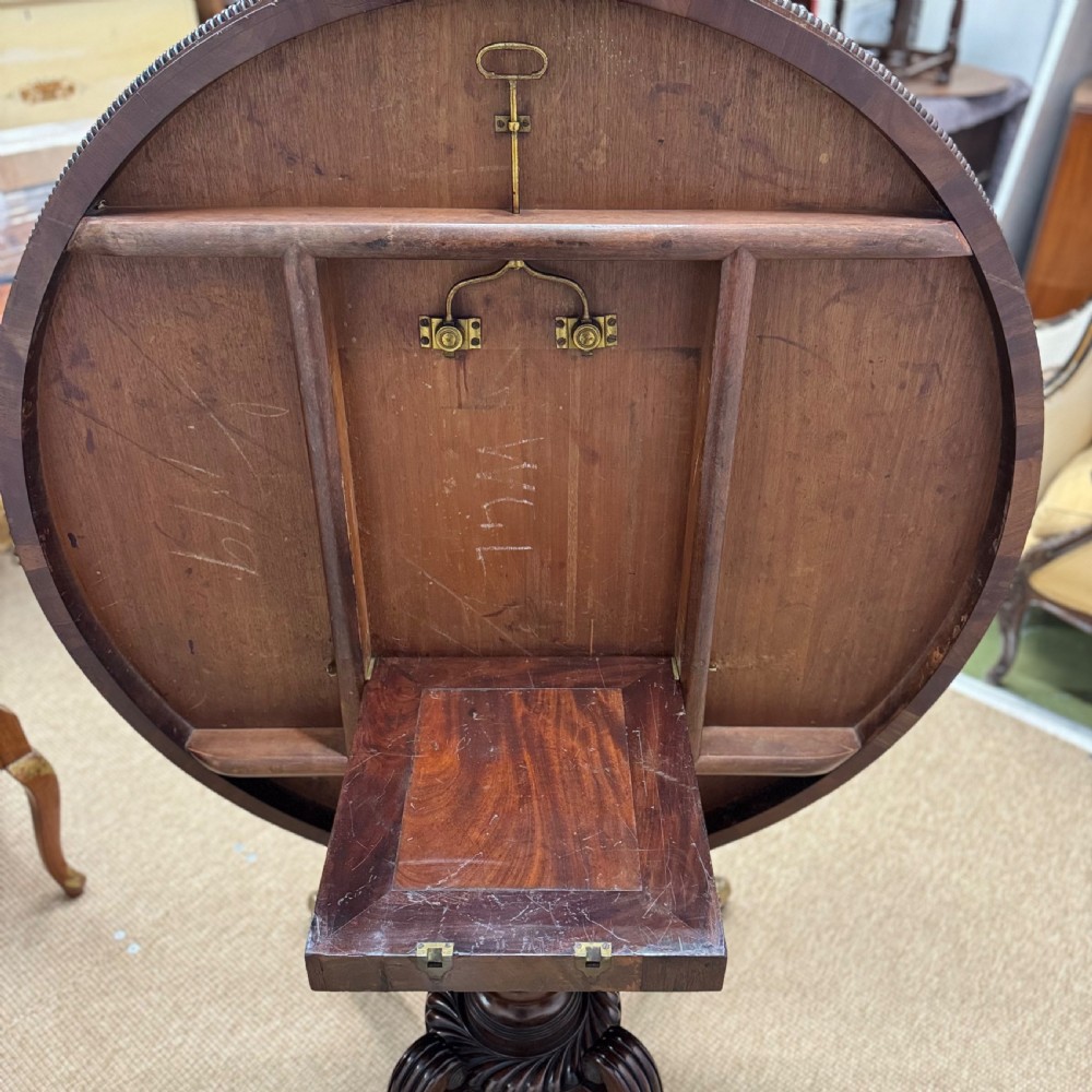 A circular Georgian plum pudding mahogany centre table shown in a tilted position on a reeded pedestal with four splayed legs and brass castors. View VII