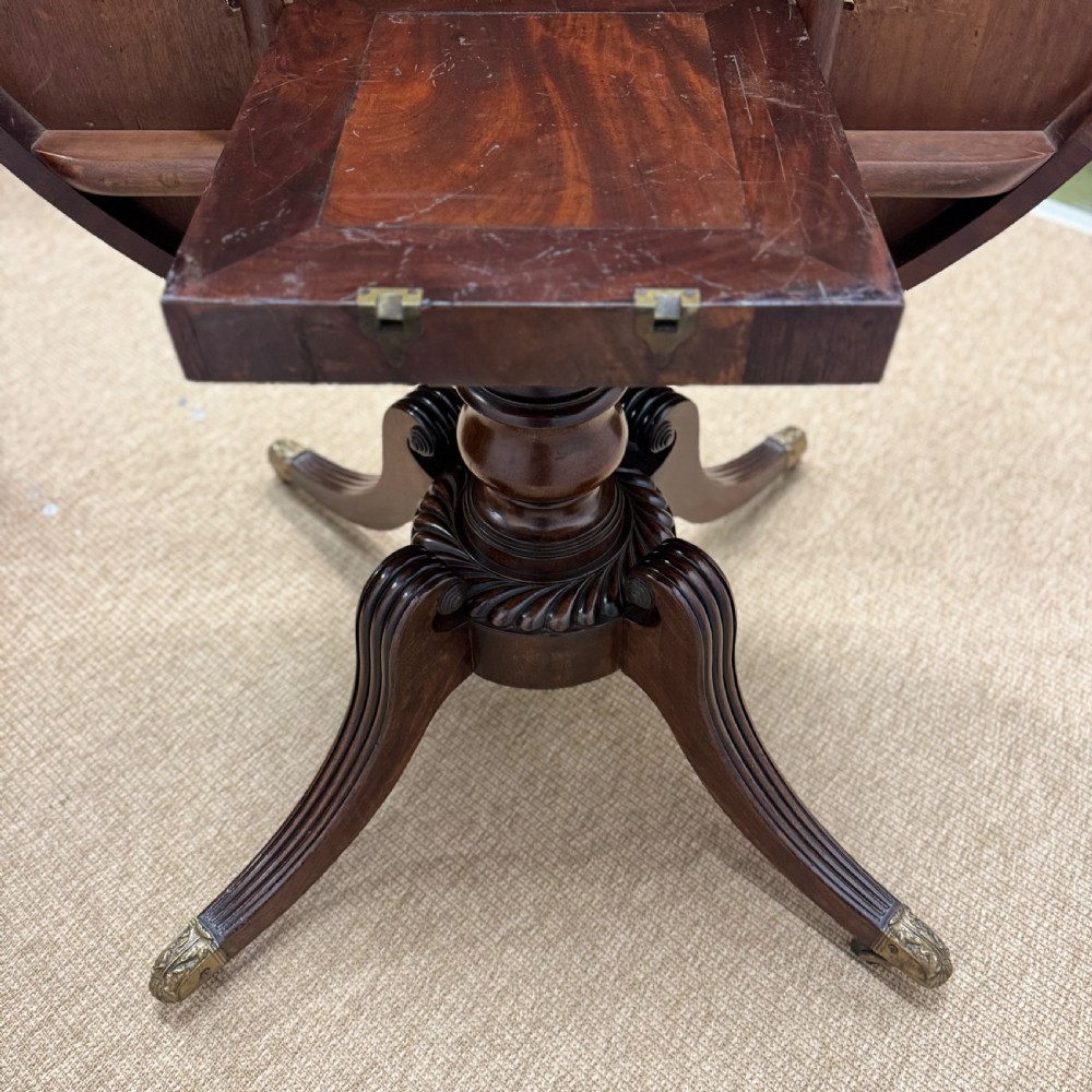A circular Georgian plum pudding mahogany centre table shown in a tilted position on a reeded pedestal with four splayed legs and brass castors. View VIII