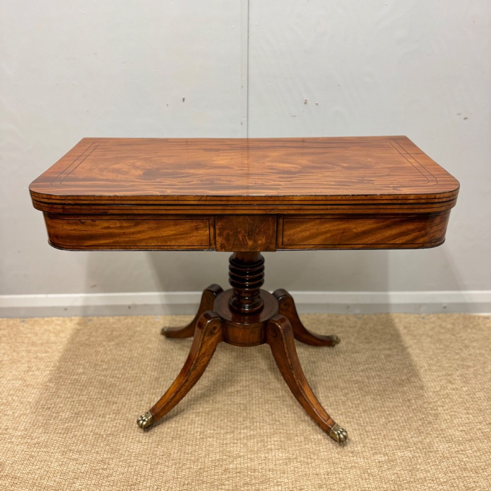 A Georgian satinwood games table featuring ebony line inlay, a turned central pedestal, and four splayed legs with brass paw feet.