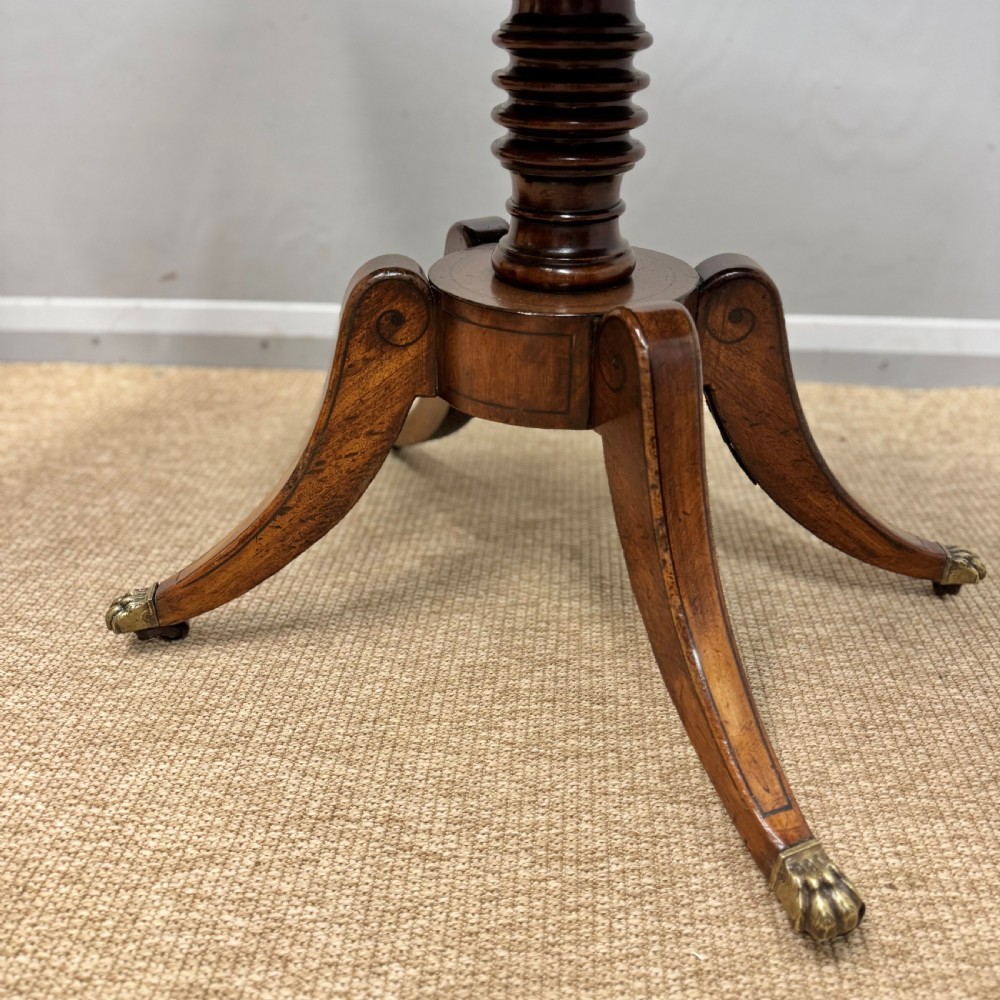 A Georgian satinwood games table featuring ebony line inlay, a turned central pedestal, and four splayed legs with brass paw feet. View III