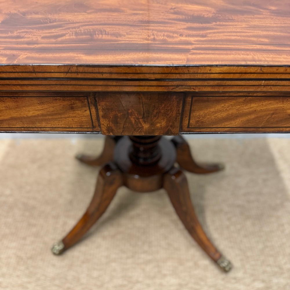 A Georgian satinwood games table featuring ebony line inlay, a turned central pedestal, and four splayed legs with brass paw feet. View V