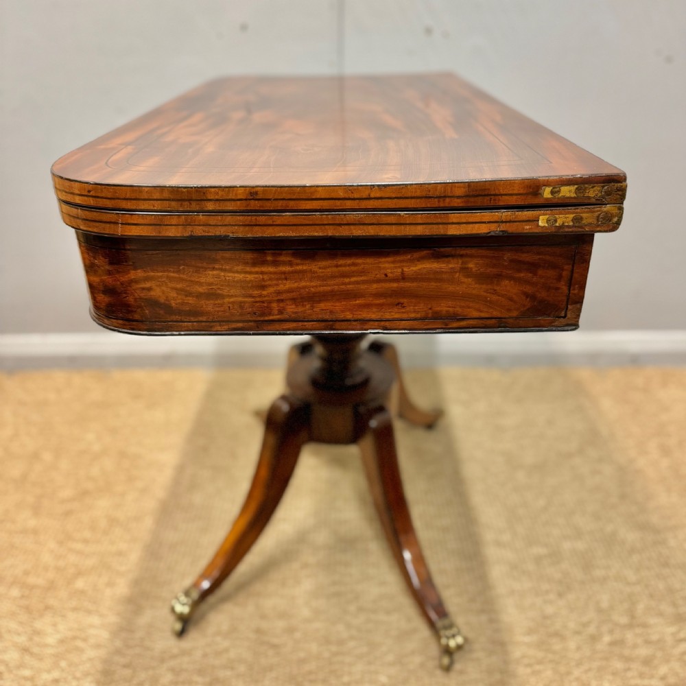 A Georgian satinwood games table featuring ebony line inlay, a turned central pedestal, and four splayed legs with brass paw feet. View VI