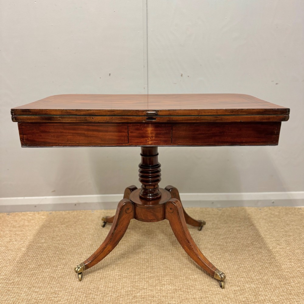 A Georgian satinwood games table featuring ebony line inlay, a turned central pedestal, and four splayed legs with brass paw feet. View VII