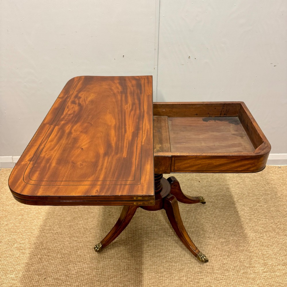 A Georgian satinwood games table featuring ebony line inlay, a turned central pedestal, and four splayed legs with brass paw feet. View VIII