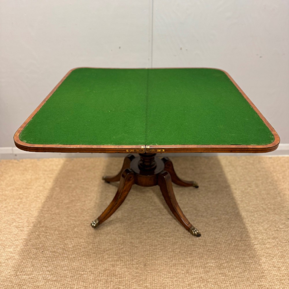 A Georgian satinwood games table featuring ebony line inlay, a turned central pedestal, and four splayed legs with brass paw feet. View IX