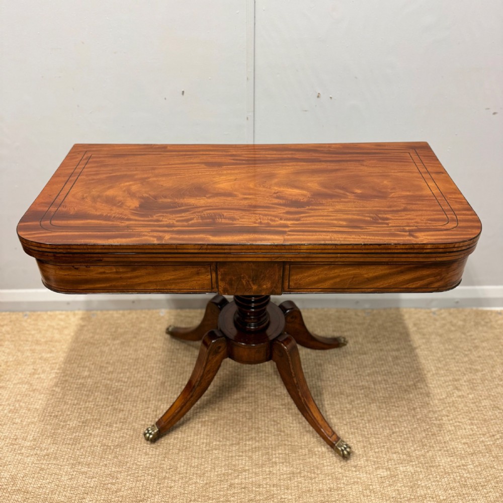 A Georgian satinwood games table featuring ebony line inlay, a turned central pedestal, and four splayed legs with brass paw feet. View X