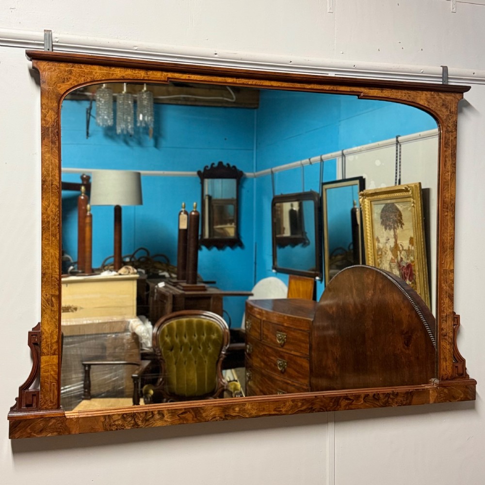 A wide antique burr walnut overmantel mirror featuring an arched upper frame, subtle stringing inlay, and stepped corner brackets.