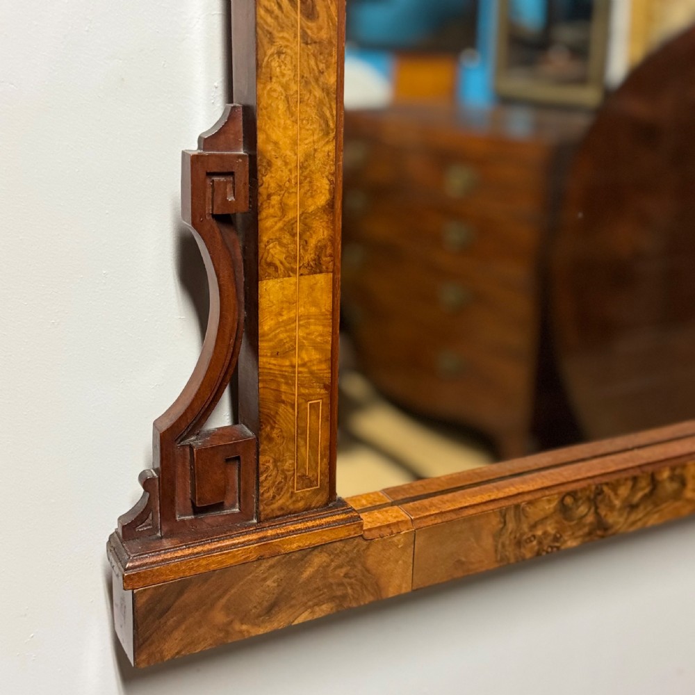 A wide antique burr walnut overmantel mirror featuring an arched upper frame, subtle stringing inlay, and stepped corner brackets. View V