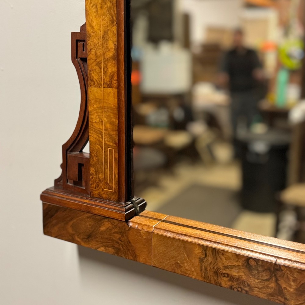 A wide antique burr walnut overmantel mirror featuring an arched upper frame, subtle stringing inlay, and stepped corner brackets. View VI