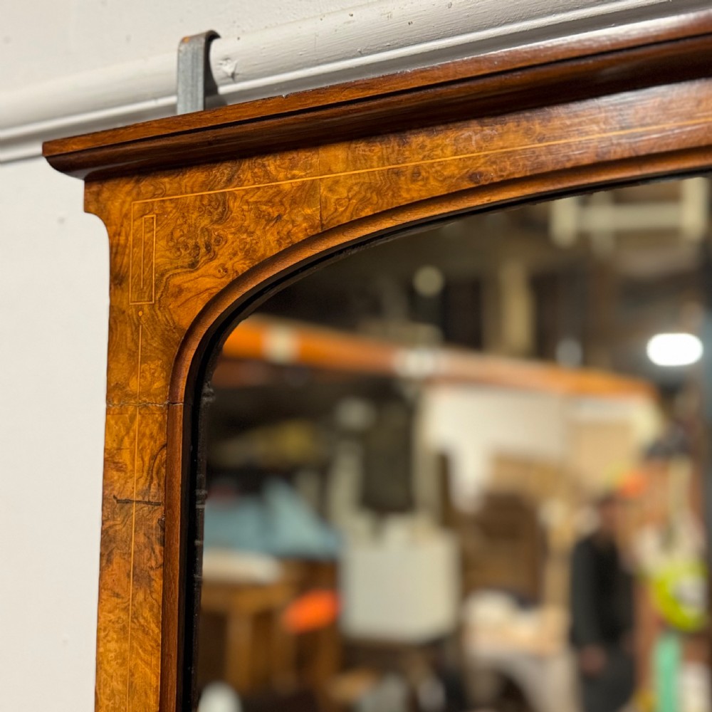 A wide antique burr walnut overmantel mirror featuring an arched upper frame, subtle stringing inlay, and stepped corner brackets. View VII