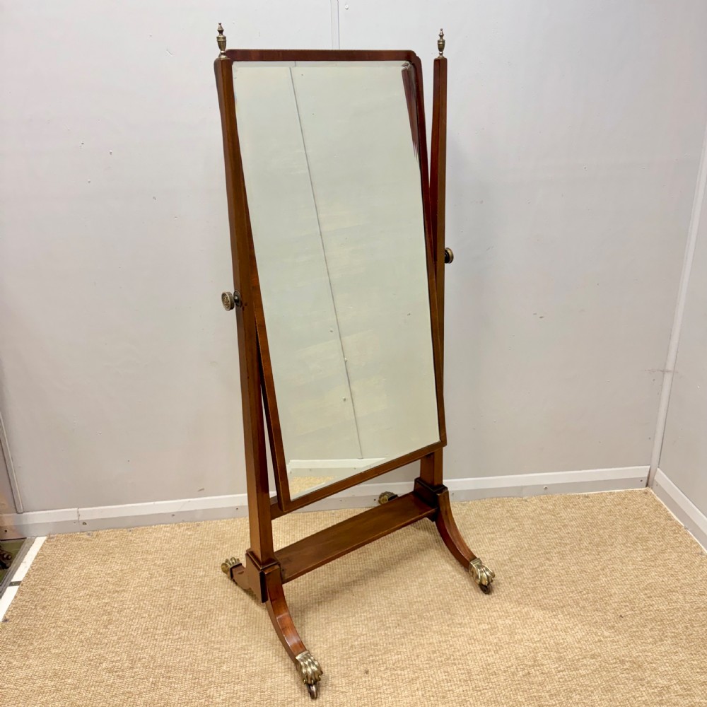 A Regency mahogany cheval mirror featuring a rectangular swivelling mirror frame, turned finials, boxwood inlay, and splayed legs ending in brass castors.