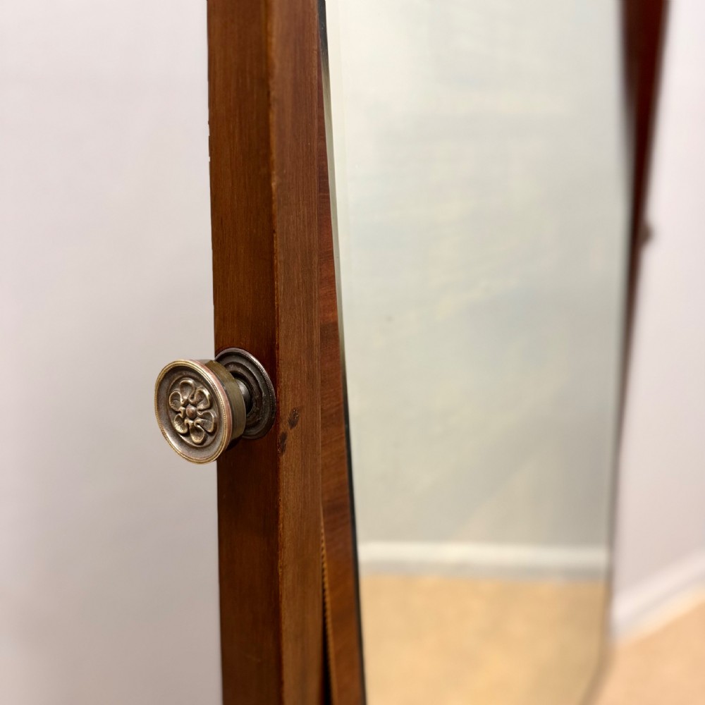 A Regency mahogany cheval mirror featuring a rectangular swivelling mirror frame, turned finials, boxwood inlay, and splayed legs ending in brass castors. View V