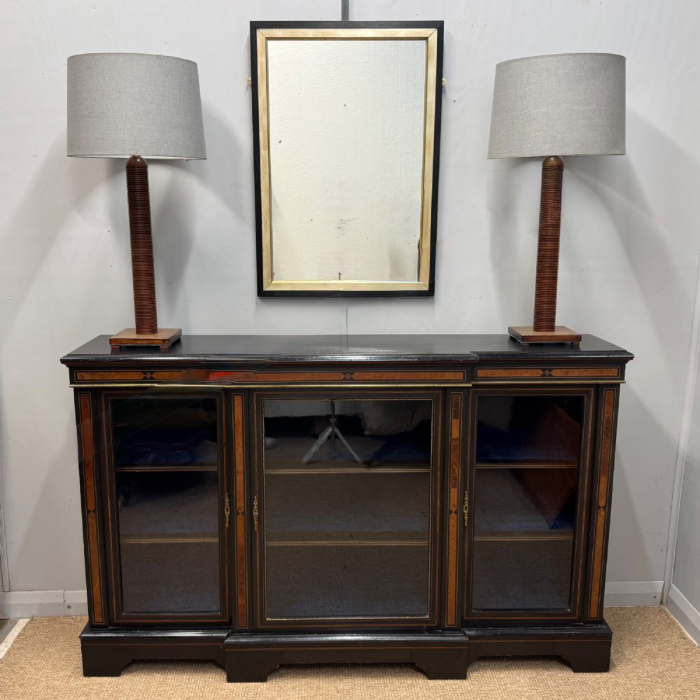 A late 19th-century low ebonised breakfront bookcase featuring three glazed doors, decorative wood inlay along the frieze and pilasters, and brass mounts. View II
