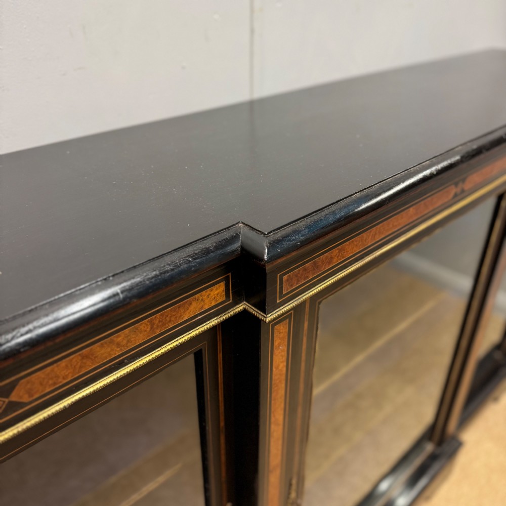 A late 19th-century low ebonised breakfront bookcase featuring three glazed doors, decorative wood inlay along the frieze and pilasters, and brass mounts. View III
