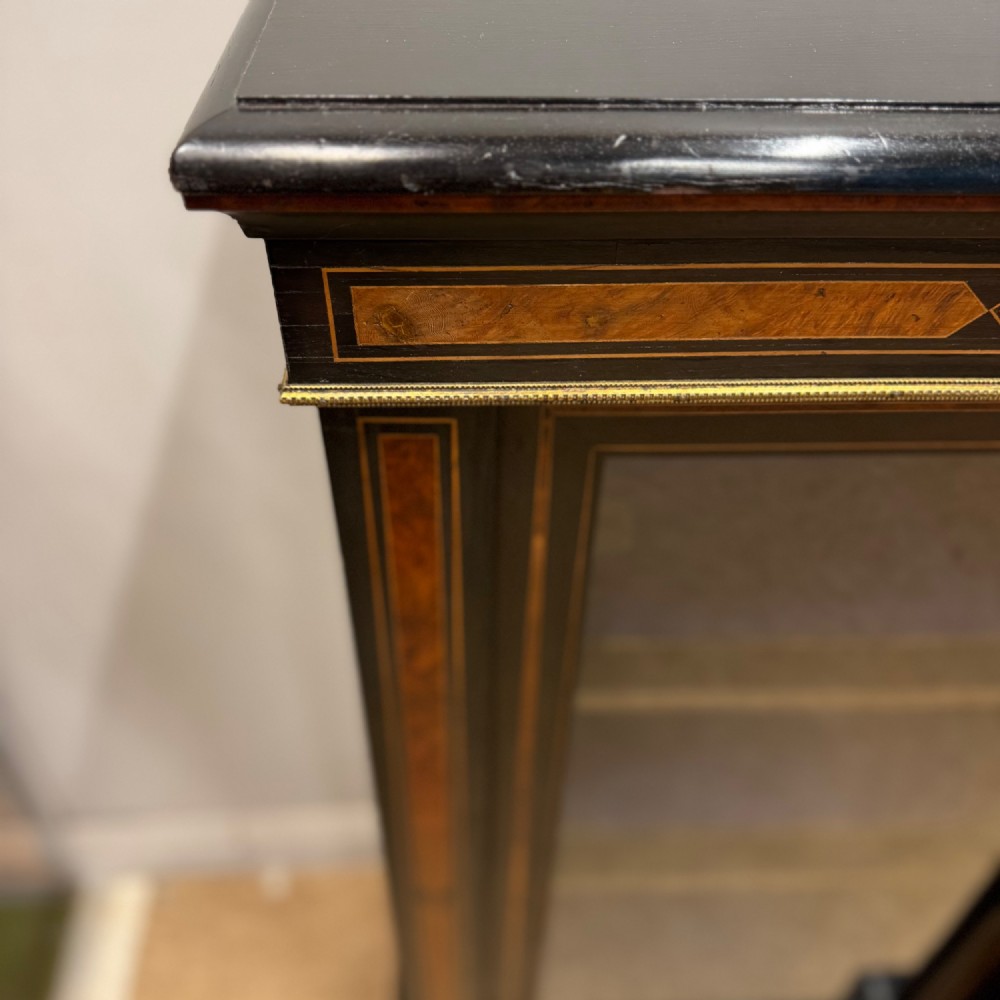 A late 19th-century low ebonised breakfront bookcase featuring three glazed doors, decorative wood inlay along the frieze and pilasters, and brass mounts. View IV