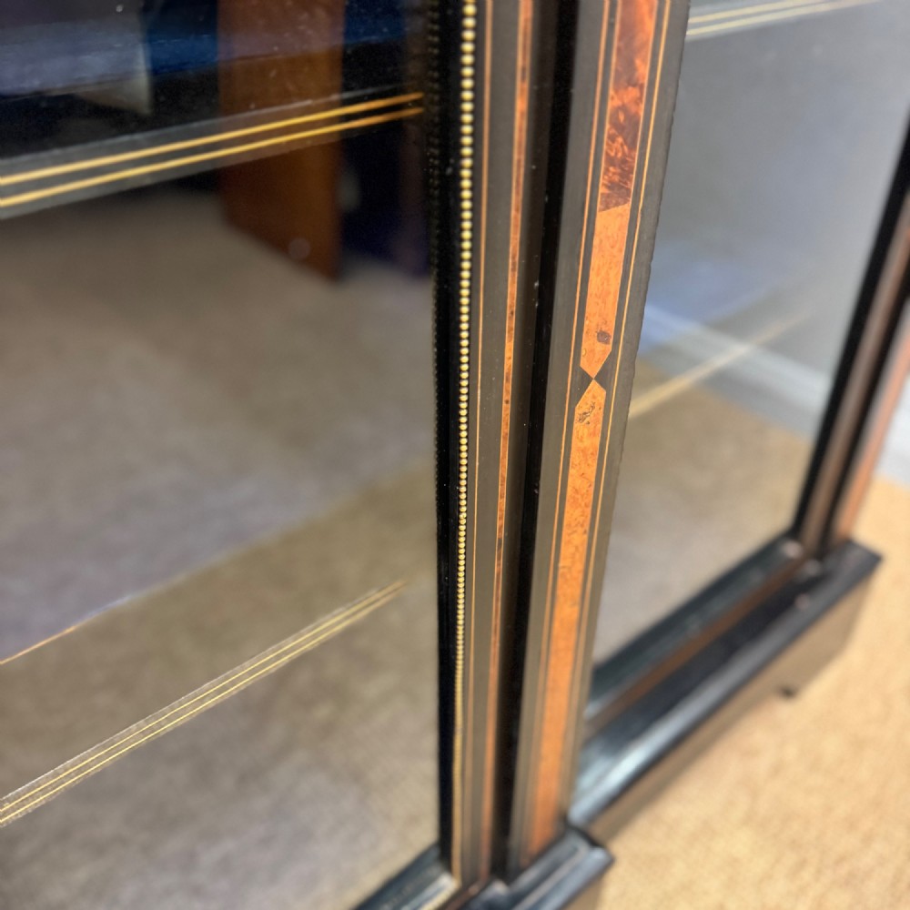 A late 19th-century low ebonised breakfront bookcase featuring three glazed doors, decorative wood inlay along the frieze and pilasters, and brass mounts. View V