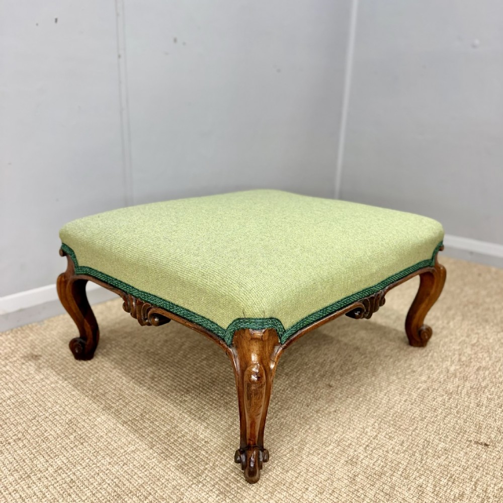 A low Victorian rosewood footstool featuring light green upholstery and hand-carved cabriole legs with scroll feet.