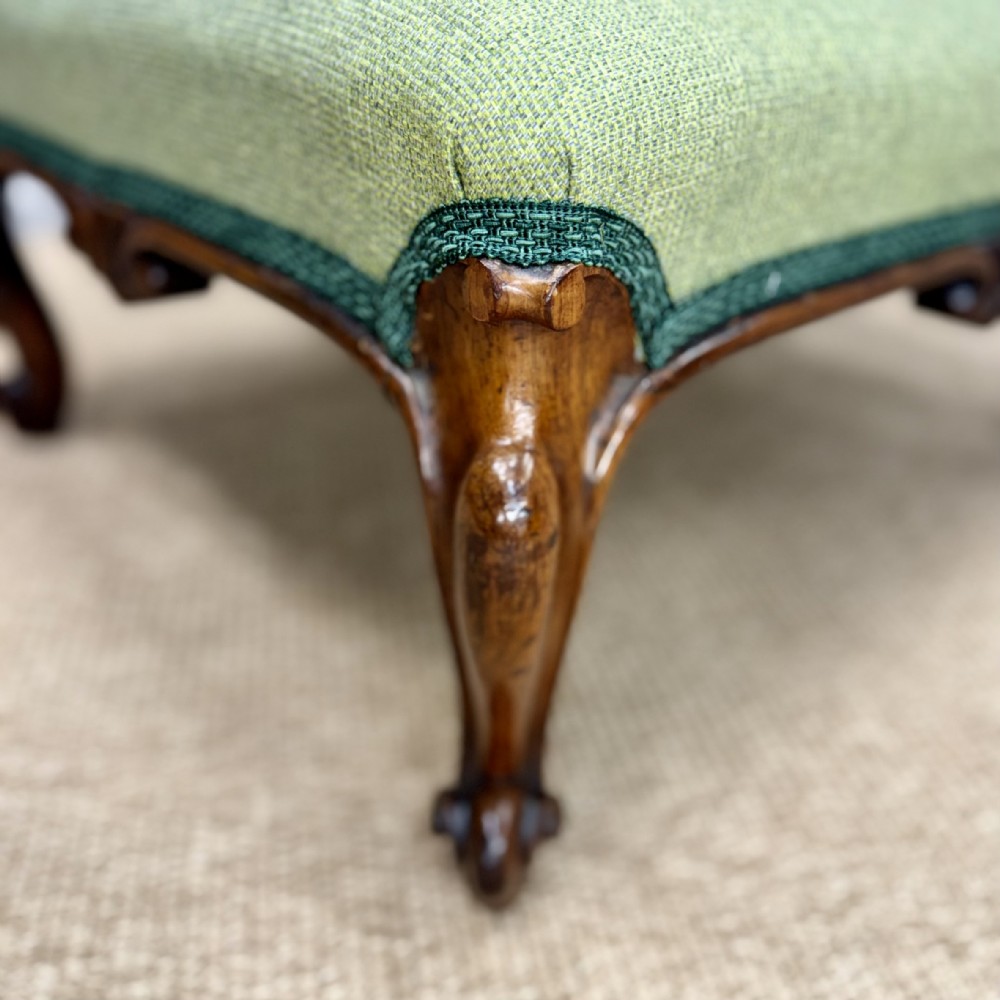 A low Victorian rosewood footstool featuring light green upholstery and hand-carved cabriole legs with scroll feet. View IV